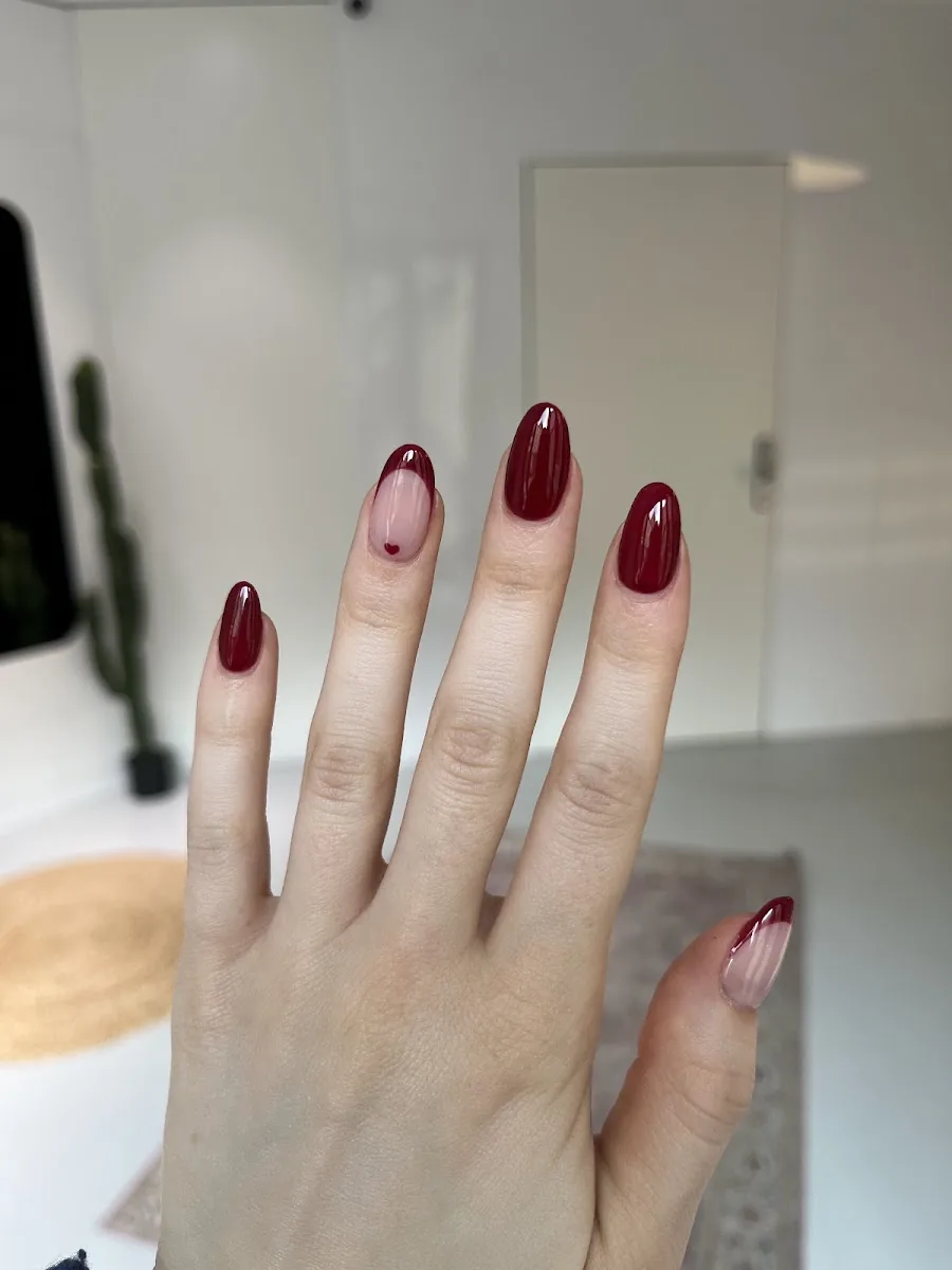 Une main de cliente aux ongles en amande vernis rouge profond, photographiée dans l'institut