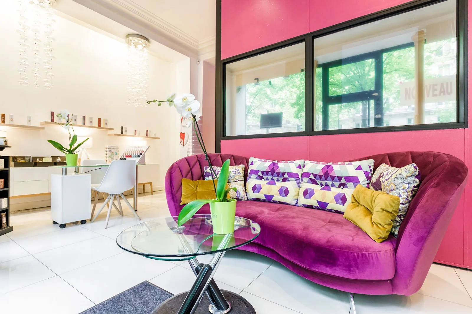 Le salon de l'institut: canapé de velours magenta et coussins à motifs contre un mur rose vif, table basse en verre et grande fenêtre donnant sur les arbres de l'avenue